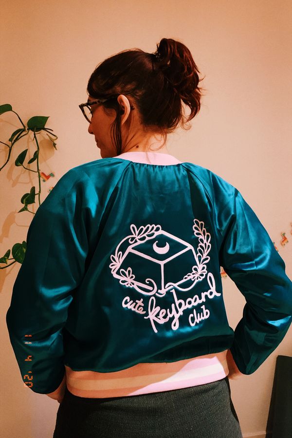 Me, with my back to the camera, wearing a teal bomber jacket, with pink embroidery at the back of a keycap and the incription: cute keyboard club.