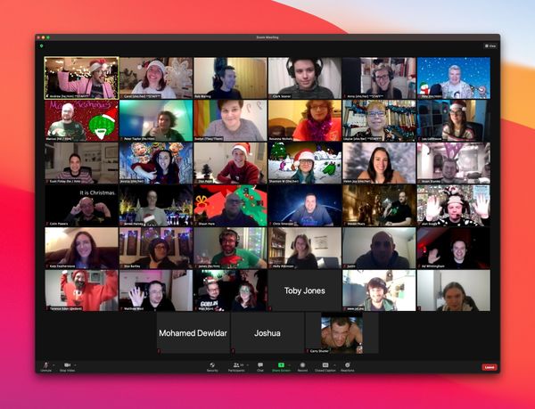 Screenshot of a zoom meeting, with around 50 smiling people with varying degrees of Christmas decorations.