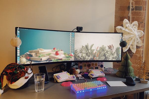 My desk, with some Christmas decorations: I put a santa hat and my reindeer glasses on the homepod, then there are a few baubles and paper trees on the right hand side. In the centre, a big monitor with a christmassy wallpaper of a pile of presents.