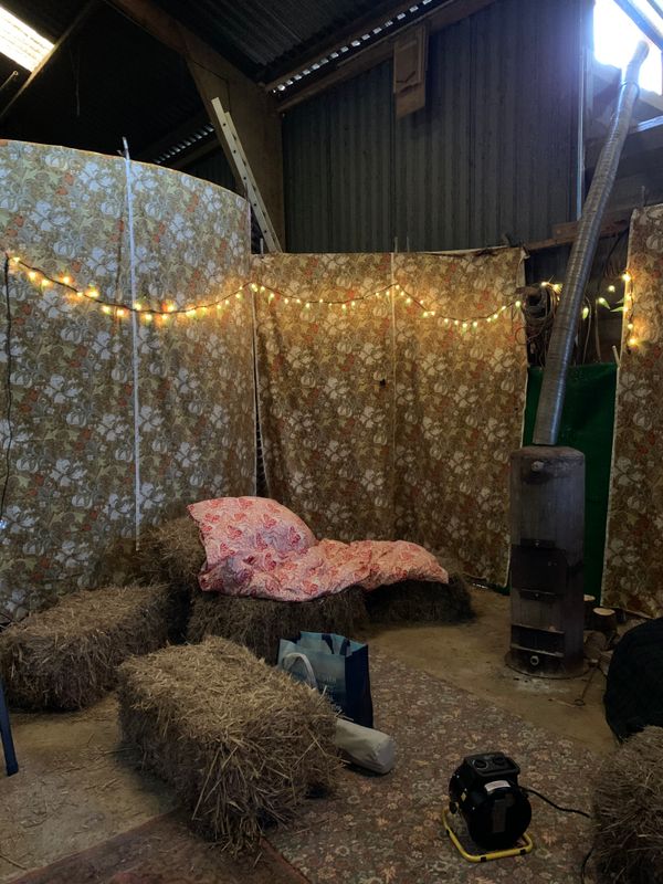 The big shed, with patterned sheets hung on the walls, some fairy lights, bales of hay as seats, and a metal wood burner in the middle.
